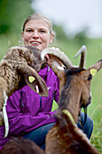 Frau sitzt bei einem Schaf und einer Ziege, Chiemgau, Bayern, Deutschland