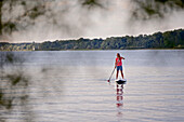 Woman stand up paddling on lake Chiemsee, Chiemgau, Bavaria, Germany