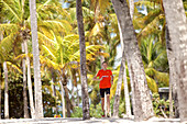 Junger Mann läuft zwischen Palmen am Strand, Dominica, Kleine Antillen, Karibik