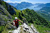 Frau im Klettersteig Via Ferrata del Centenario vor Menaggio (rechts) und Varenna (links) am Comer See und Grigna Settentrionale (2408 m) darüber, Italien