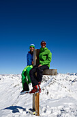 Two men sitting on the summit cross of the Schwarzhorn (3147 m), Grisons, Switzerland, Europe