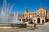 Two young women sit next to fountain at Plaza de Espana in Maria Luisa Park, Seville, Andalusia, Spain