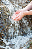 Child holding cupped hands under fresh, flowing water, cropped