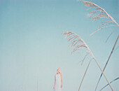 Woman standing in the distance, focus on tall grass in foreground