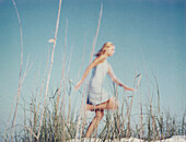 Young woman running through tall dune grass, side view
