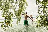 two young men going swimming in Lake Starnberg near a birch tree, Berg, Upper Bavaria, Germany