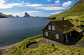 Traditional house with a grass covered roof in Bour, Vagar Island. Islands Tindholmur and Drangarnir in the background, Faroe Islands