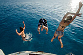 Two young women and a young man are jumping from the stern of a sailing yacht into the clear blue sea, Mallorca, Balearic Islands, Spain, Europe