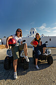 Two young women sitting on quad bikes and smiling into the camera, Greek Islands, Aegean, Cyclades, Greece