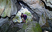 Young woman looking into cave in which food has been stored, Selvaggio Blu, Sardinia, Italy, Europe