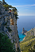 Eine junge Frau wandert entlang der gebirgigen Küste, Felsnadel bei Pedra Longa im Hintergrund, Punta Giradili, Selvaggio Blu, Sardinien, Italien, Europa