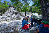 Junge Frau mit Trekkingausrüstung bespricht den Weg auf einer Wanderkarte mit Einheimischen, bei einer Ovile, einer traditionellen Hirtenhütte, Selvaggio Blu, Sardinien, Italien, Europa
