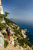 A young woman with trekking gear hiking along the mountainous coast above the sea, Golfo di Orosei, Selvaggio Blu, Sardinia, Italy, Europe
