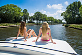 Two Young women wearing a bikini relaxing on the deck of a Le Boat Royal Mystique houseboat on the Plassendale - Niuewpoort canal, near Bruges, Flemish Region, Belgium