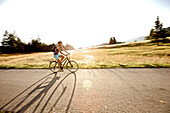 Junge Frau fährt mit ihrem Fahrrad bei einer Wiese an einem sonnigen Tag, Tannheimer Tal, Tirol, Österreich