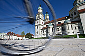 Young female cyclist in front of a church, St. Lorenz Basilica, Kempten, Bavaria, Germany