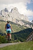 Young woman riding her bike near mountains on a sunny day, Rote Floeh, Gimpel, Hochwiesler, Tannheimer Tal, Tyrol, Austria