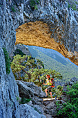 Woman hiking Selvaggio Blu crossing arch, Selvaggio Blu, National Park of the Bay of Orosei and Gennargentu, Sardinia, Italy