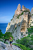Frau wandert am Selvaggio Blu an Felstürmen vorüber, Selvaggio Blu, Nationalpark Golfo di Orosei e del Gennargentu, Sardinien, Italien