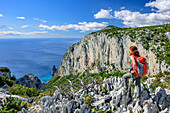 Woman hiking Selvaggio Blu looking at coast of Golfo di Orosei with rock spire Pedra Longa, Selvaggio Blu, National Park of the Bay of Orosei and Gennargentu, Sardinia, Italy