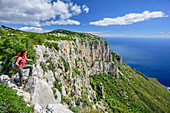 Woman hiking Selvaggio Blu standing at cliff and looking at coast of Golfo di Orosei, Selvaggio Blu, National Park of the Bay of Orosei and Gennargentu, Sardinia, Italy