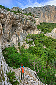 Woman hiking Selvaggio Blu beneath cliff, Selvaggio Blu, National Park of the Bay of Orosei and Gennargentu, Sardinia, Italy