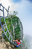 Woman ascending on ladder to Steineberg, fog in background, Steineberg, Nagelfluh range, Allgaeu Alps, Allgaeu, Svabia, Bavaria, Germany