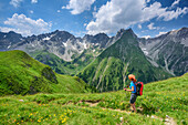 Frau wandert durch Blumenwiese mit Griesslspitze, Rotspitze und Freispitze im Hintergrund, Lechtaler Alpen, Tirol, Österreich