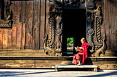 Asian monk reading by ornate doorway to temple, Mandalay, Mandalay, Myanmar