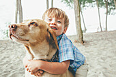 Boy hugging dog on wooded beach, Seattle, WA, USA