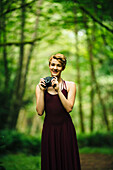 Caucasian woman holding camera in forest, C1