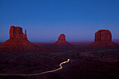 Long exposure of car driving past butte rock formations in desert landscape, Monument Valley Tribal Park, Utah, United States, C1