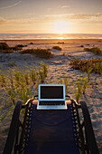 Laptop on deck chair overlooking sunset on beach, C1