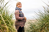 Caucasian pregnant woman holding her stomach on beach, Cannon Beach, Oregon, United States