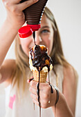 Messy Caucasian girl pouring chocolate syrup on ice cream cone, Jersey City, New Jersey, USA