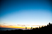 Silhouette of family on rural hillside at sunset, Cannon Beach, Oregon, United States