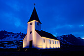 White church illuminated near snowy mountains at night, Vik, Sudhurland, iceland