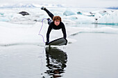 Caucasian surfer leaping on board in glacial water, Jokulsarlon, Iceland, Iceland