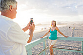 Caucasian man taking photograph of wife on boardwalk at beach, Santa Monica, California, USA