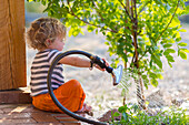 Caucasian baby boy watering plants from back patio, Santa Fe, New Mexico, USA