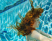 Teenage girl with red hair swimming underwater in pool, Bainbridge Island, WA, United States