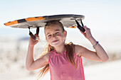 Caucasian girl carrying sled on sand dune, White Sands, New Mexico, USA