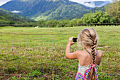 Caucasian girl taking photograph of rural meadow, Kauai, Hawaii, USA