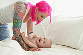 Caucasian mother with pink hair and tattoos playing with baby, Toronto, Ontario, Canada