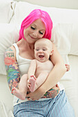 Caucasian mother with pink hair and tattoos cradling baby, Toronto, Ontario, Canada