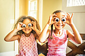 Mixed race sisters playing with googly eyes, C1