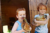 Two young ginger children carrying chickens in the country