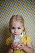 A 2 years old girl posing as she 's drinking a glass of milk