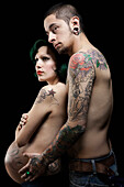 Tattooed Hispanic man hugging tattooed, pregnant wife