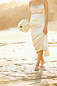 Caucasian bride holding bouquet on beach